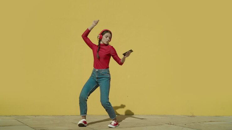 Young Happy Latin Woman makes dancing cool moves wearing a red shirt and jeans and red converse shoes with a yellow background wall on a sunny day wide-angle shot in slow motion