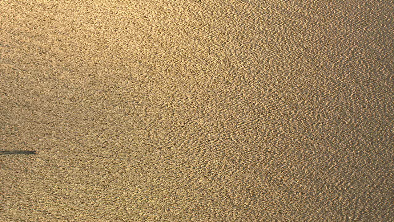 el sol poniente se refleja en el mar, un bote pequeño que pasa por la pantalla