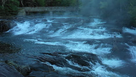 Aerial-drone-shot-in-slow-motion-over-the-dark-rocks-and-misty-waterfall-at-Big-Wilson-Falls-during-dusk-in-Maine