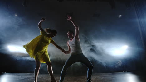 two dancers a man and a woman run to each other and a male partner raises a woman in a yellow dress in her arms and rotates in the air performing top support.