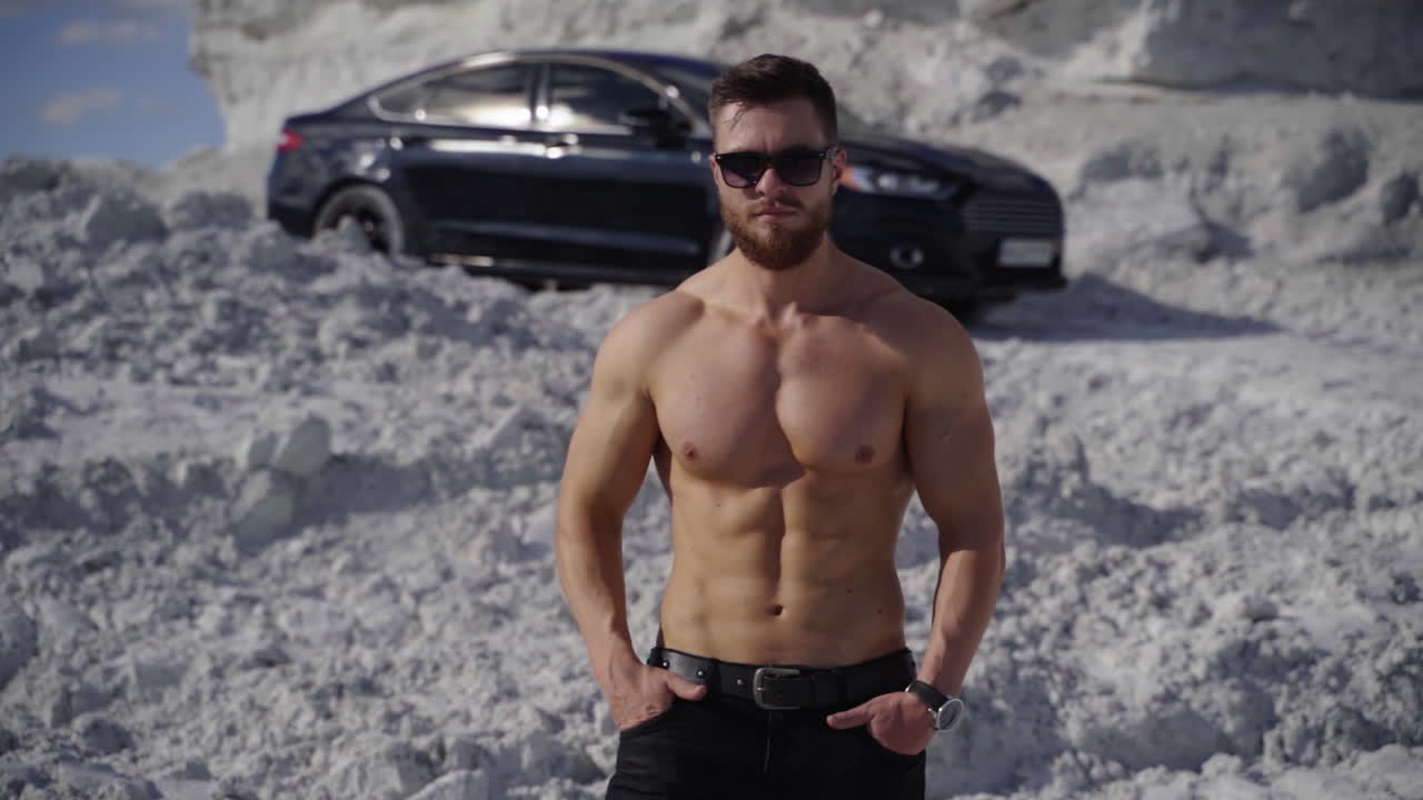 Muscular man on black car background. Strong man without shirt walking on white canyon in at sunlight. Portrait of handsome athlete outdoors.