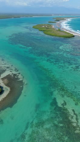 turquoise and blue shallow waters, playa caobita, dominican republic. aerial drone forward tilt-up reveal, vertical format