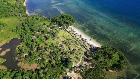 aerial flyover shot of tropical island bagasbas beach resort during daytime with lush greenery and vibrant sea waters at catanduanes, philippines.