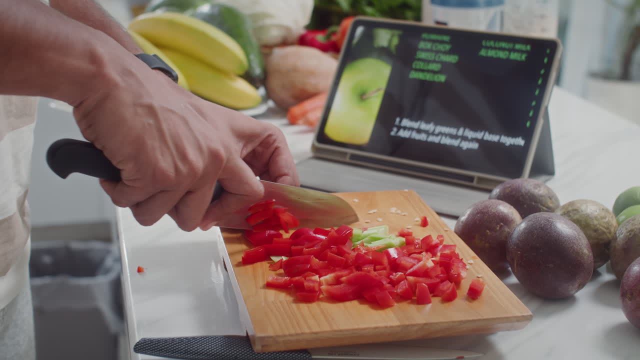 Person Cutting Vegetables for Smoothie Using Recipe on Tablet
