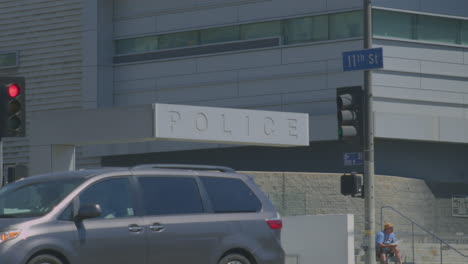 a man sitting and reading in front of police station, facing busy road traffic with moving cars