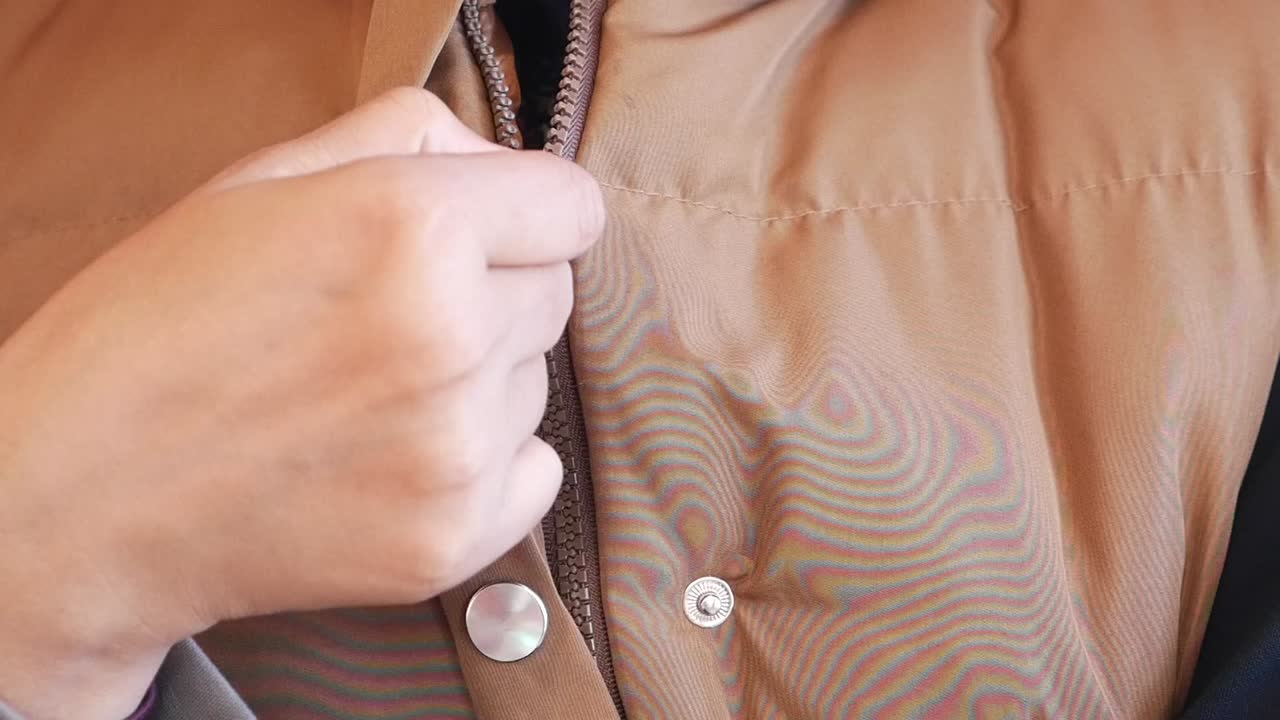 primer plano de una persona abriendo la cremallera de una chaqueta puffer marrón