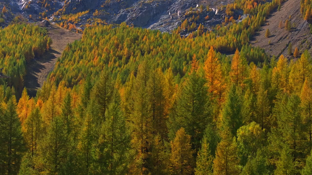 Stunning aerial footage of Saas-Fee in autumn. Golden forests surround the alpine village, nestled in the Swiss Alps. Vibrant fall colors and majestic peaks highlight the beauty of the season.