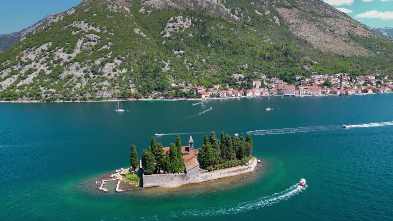 Aerial drone view of Sveti Dorde Island - Saint George Monastry in the middle of the island. In background is Perast city. Famous travel destination in Montenegro. Static footage. Boats passing.