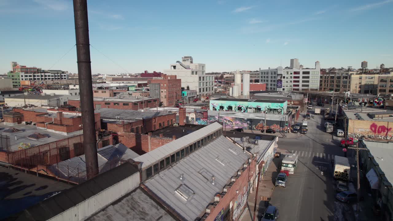 Gritty graffiti covered industrial buildings in Bushwick, Brooklyn, NY. Drone shot with factory smokestack in foreground, 4K