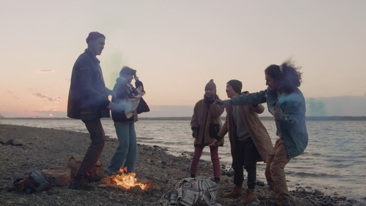 Group Of Teenage Friends Dancing Around A Bonfire Holding Colored Sparklers On The Seashore