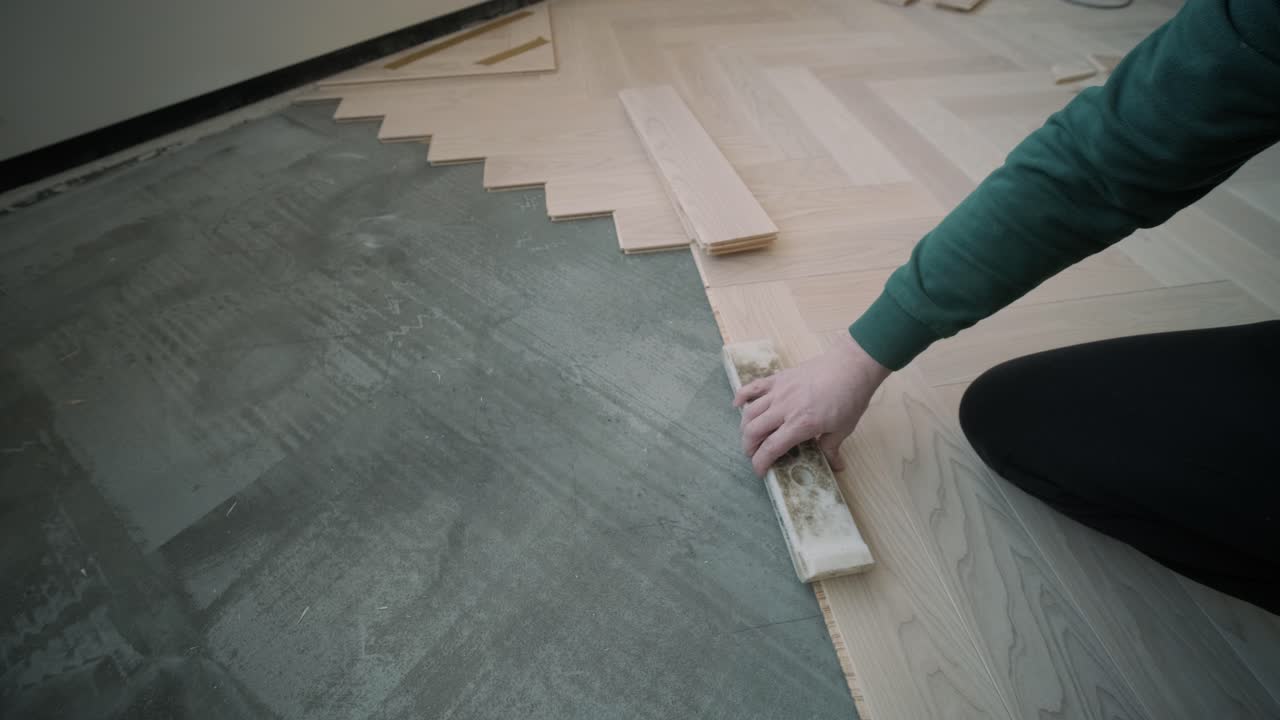 Worker installing wooden flooring with hammer and tapping block