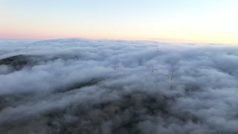 Drone-aerial-footage-of-low-clouds-moving-across-a-field-with-wind-turbines-at-sunset-in-Madeira-island,-Portugal