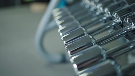 Shiny-metallic-dumbbell-rack-at-indoor-gym-facility-with-blurry-background