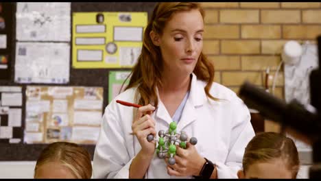 teacher assisting school kids with molecule model in laboratory