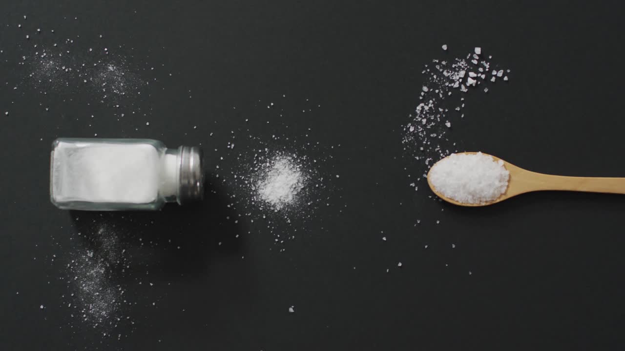 Video of salt in a salt shaker and spoon on black background