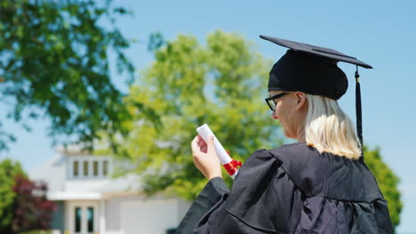 Student-Absolvent-In-Mantel-Und-Mütze-Vor-Dem-Hintergrund-Seines-Hauses