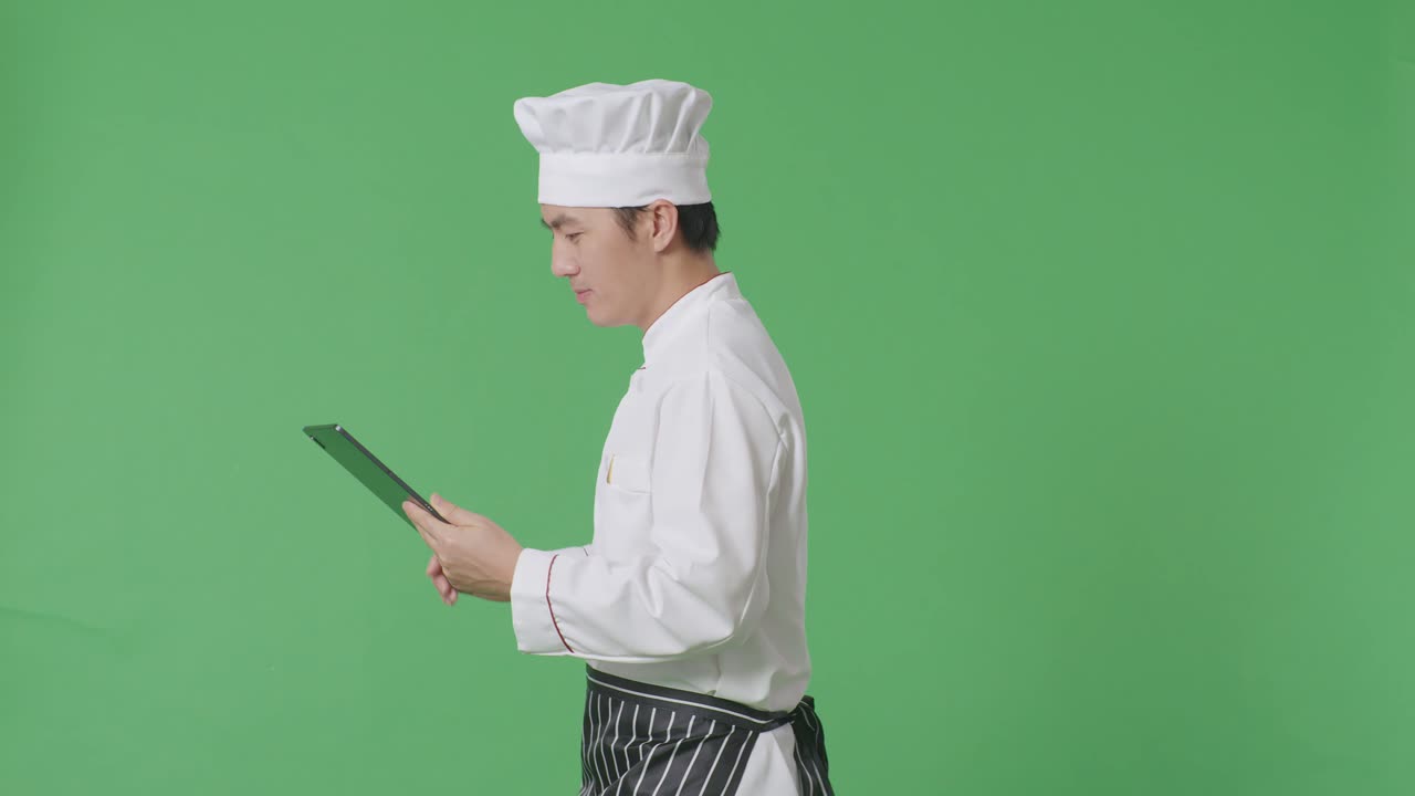 녹색 화면 배경 스튜디오에서 는 동안 태블릿을 사용하는 아시아 남자 셰프의 측면 시각
