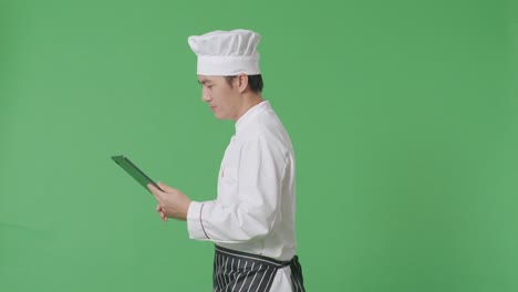 side view of asian man chef using a tablet while walking in the green screen background studio