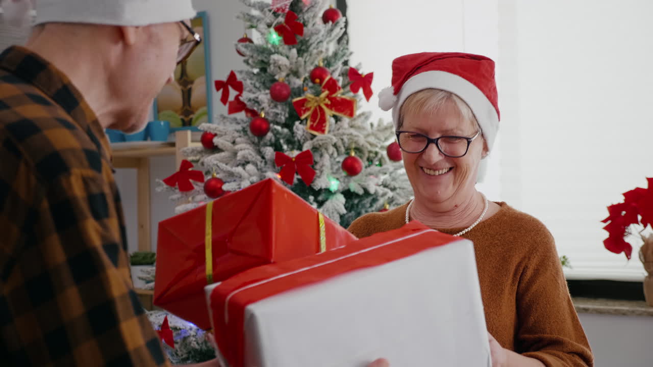 una pareja de mayores feliz disfrutando de la navidad compartiendo un regalo de envoltura en la cocina decorada de navidad