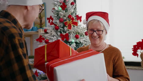 happy senior couple enjoying christmastime sharing wrapper gift present in xmas decorated kitchen