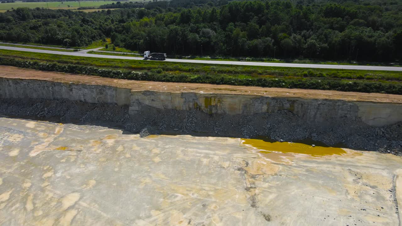 Riprese aeree con drone che sorvolano una ripida scogliera calcarea mineraria che si trova accanto a un'autostrada o strada rurale di campagna dove il traffico è visibile. Natura verdeggiante e coperta di alberi tutt'intorno