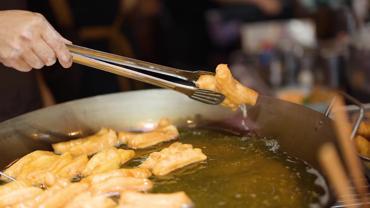 Gros plan sur des mains utilisant des pinces métalliques pour retourner de la pâte frite dorée dans de l'huile bouillonnante.