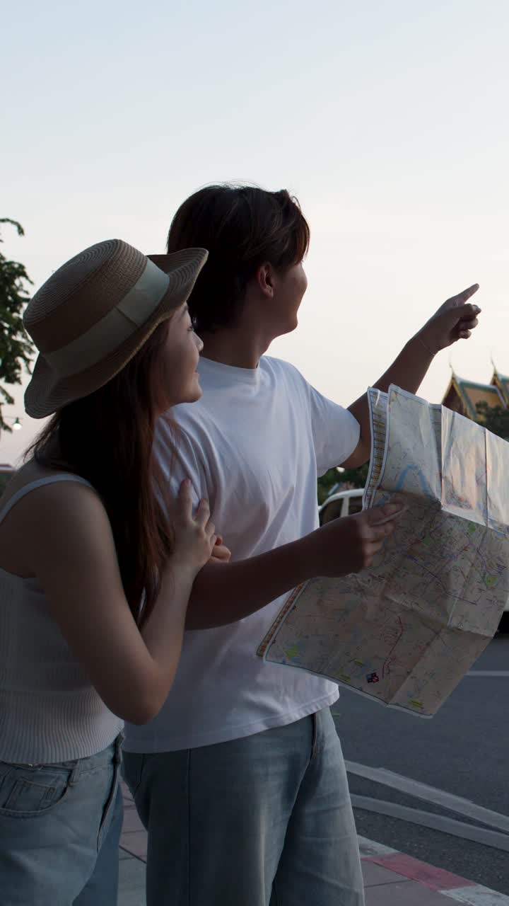 Giovani turisti studiano una mappa cartacea su una strada urbana al tramonto, indicando un punto di riferimento del tempio.