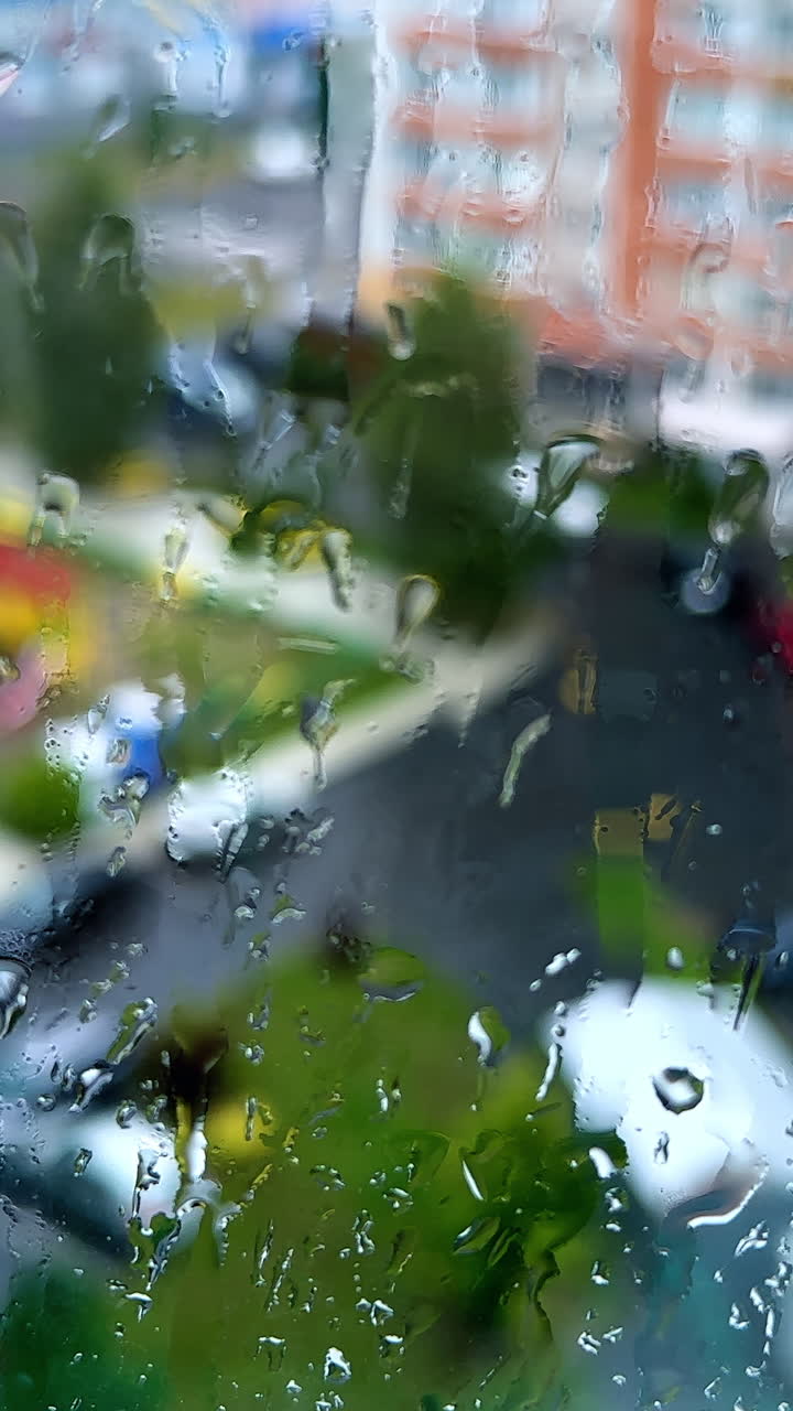 View on the yard in residential area through the window covered with rain drops. Sight of the street from high rise floor of multistoried building.. Vertical video