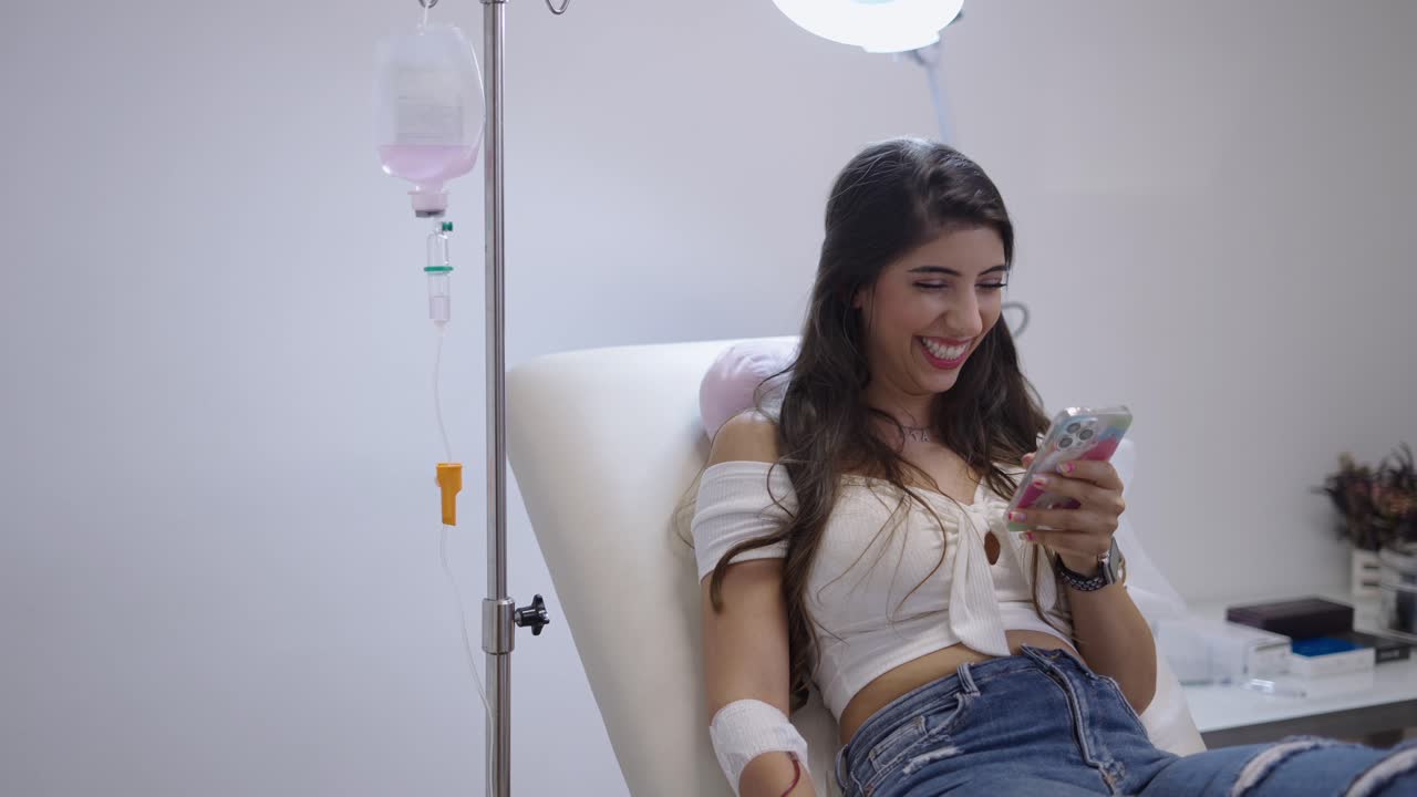 Donna che riceve un trattamento con flebo mentre usa il suo smartphone in una clinica