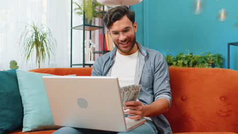 hombre feliz sonriente contando dinero en efectivo y usar computadora portátil calcular los ingresos domésticos ganancias en casa