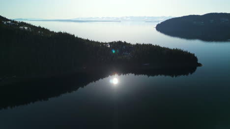 Aerial-view-of-still-reflecting-water-and-forested-islands-with-snow,-in-Alaska