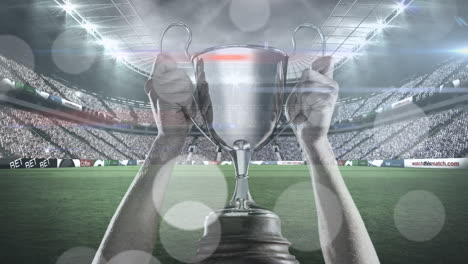 animation of spots of light over caucasian man holding silver cup in sports stadium