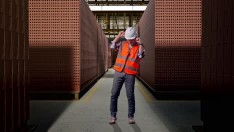 full body of asian male engineer with safety helmet screaming goal and dancing celebrating with red brick packed in stacks are stored