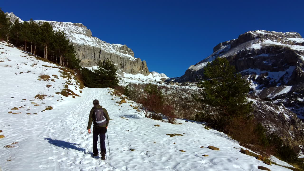 hombre haciendo senderismo de invierno entre las montañas nevadas de los pirineos españoles con un cielo azul