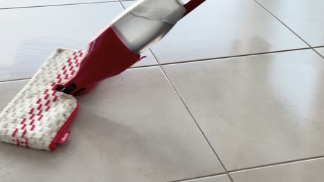 a red spray mop glides over glossy kitchen floor tiles, cleaning water with smooth, steady movements in bright natural daylight