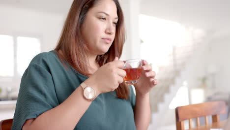 Mujer-Birracial-Enfocada-De-Talla-Grande-Bebiendo-Té-Mientras-Usa-Una-Computadora-Portátil,-Trabajando-Desde-Casa,-Cámara-Lenta