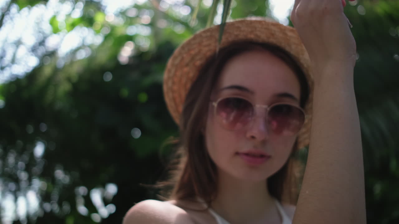 женщина в соломенной шляпе и солнцезащитных очках в тропическом саду