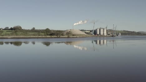 Planta-De-Cemento-A-Orillas-Del-Río-En-Irlanda-Con-Una-Gran-Pila-De-Humo-Vista-Más-Allá