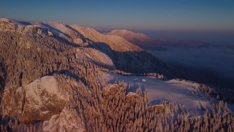 Immerse-in-the-breathtaking-winter-landscape-as-the-drone-glides-over-snow-covered-trees-on-the-mountain-peak,-beneath-a-sea-of-clouds