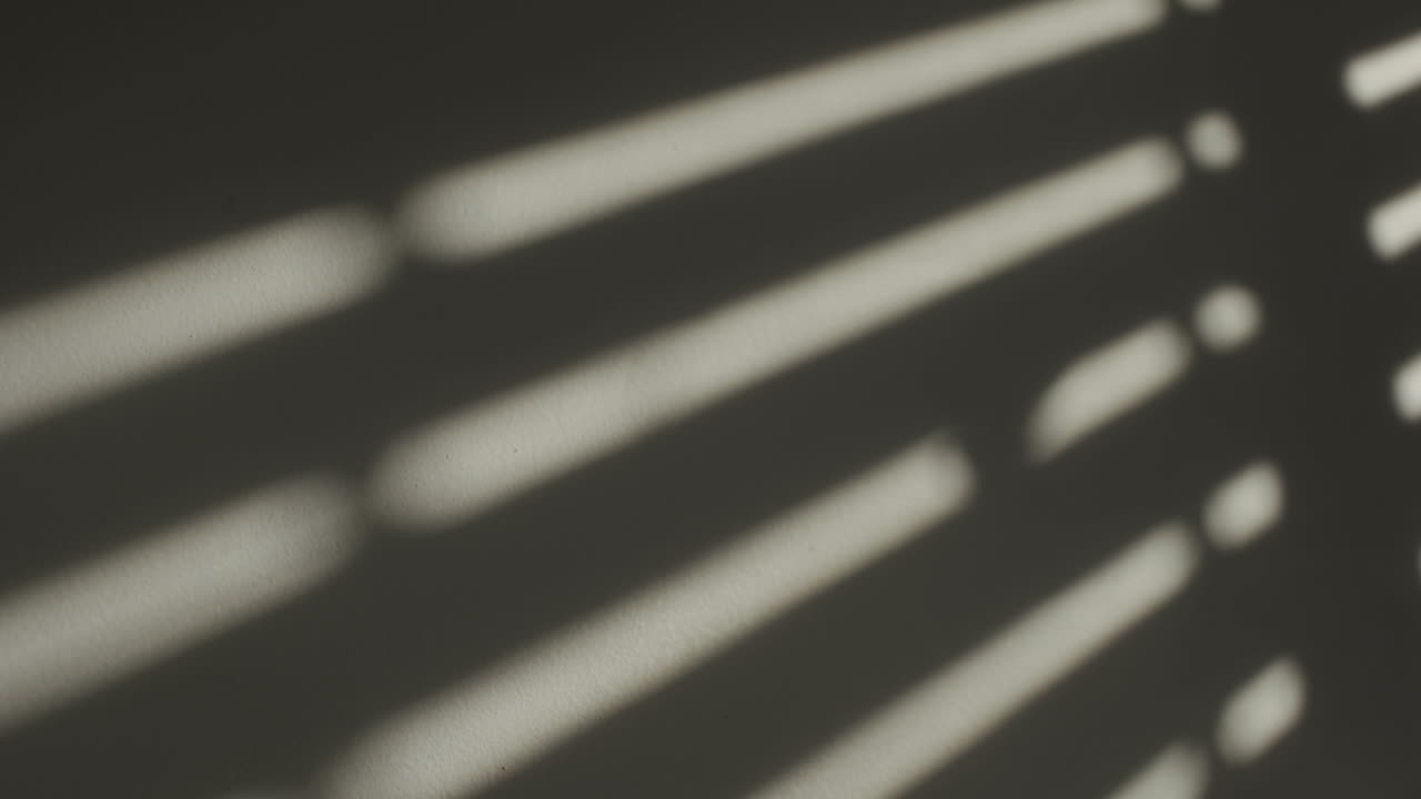 тени от закрывающейся оконной ставни на белой стене комнаты