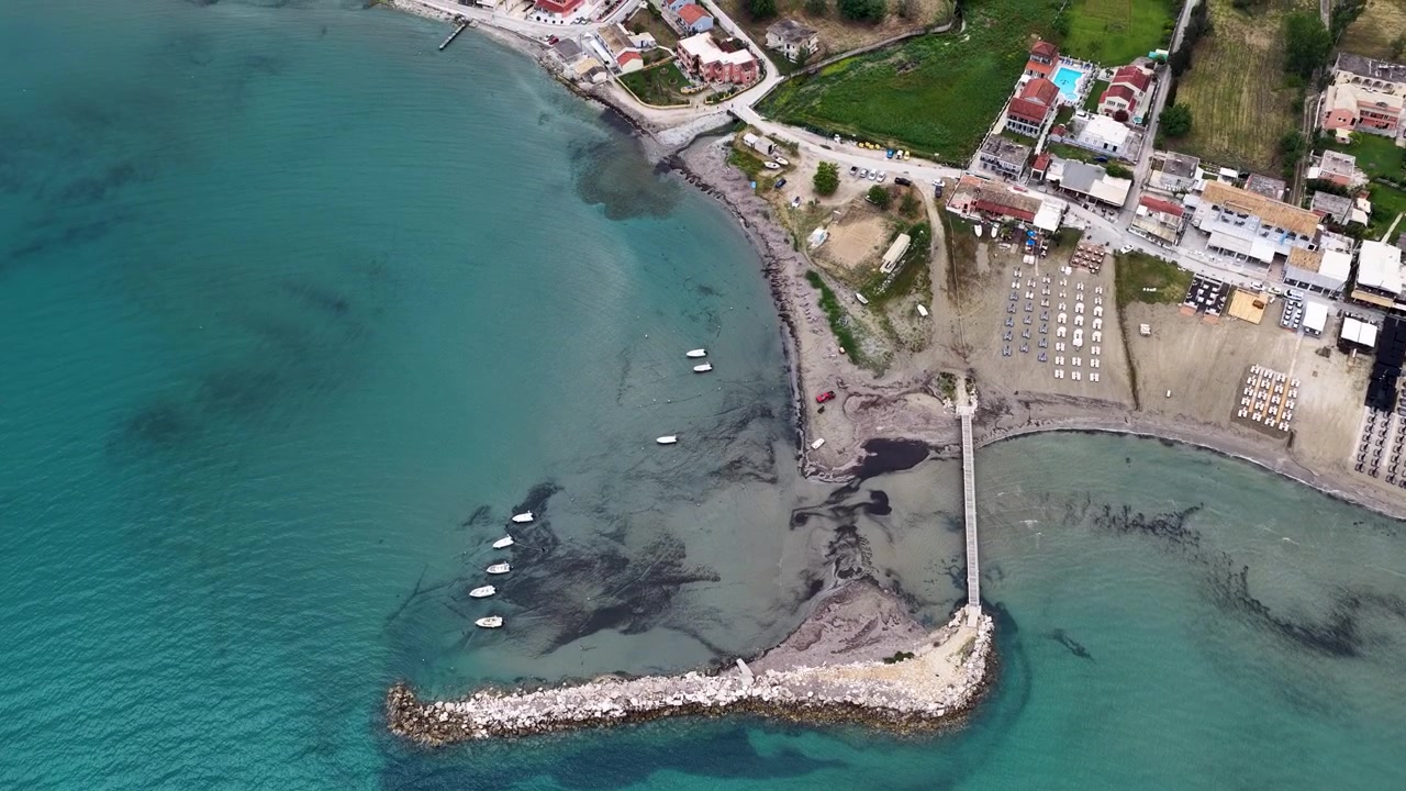 Veduta aerea del molo della spiaggia di Roda con piccole imbarcazioni nel mare Ionio turchese, Corfù settentrionale, Grecia. Volo di drone su una località balneare costiera con spiaggia sabbiosa e frangiflutti.