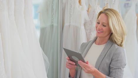 mature female owner of bridal wedding dress shop with digital tablet