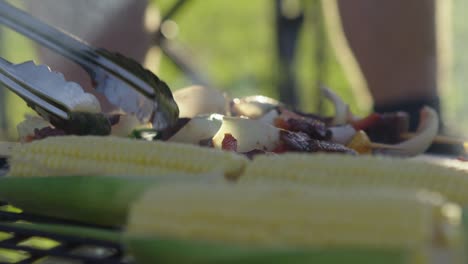 Volteando-Brochetas-En-Una-Barbacoa-Con-Verduras-En-Primer-Plano