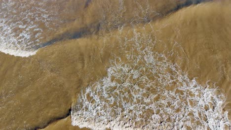 aerial footage of waves gently breaking on the beach, with golden sand