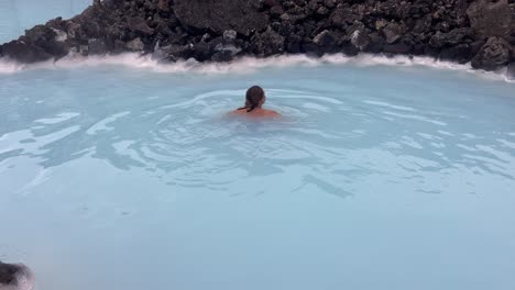 pretty female swimming happily in a volcanic blue water thermal spa