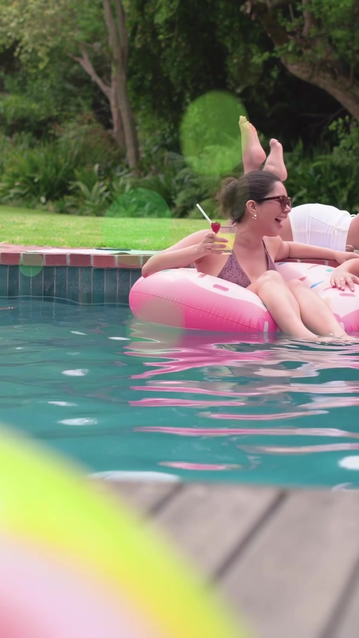 Vertical video: Woman on pink float turning at friend laugh holding drink with green overlay ad