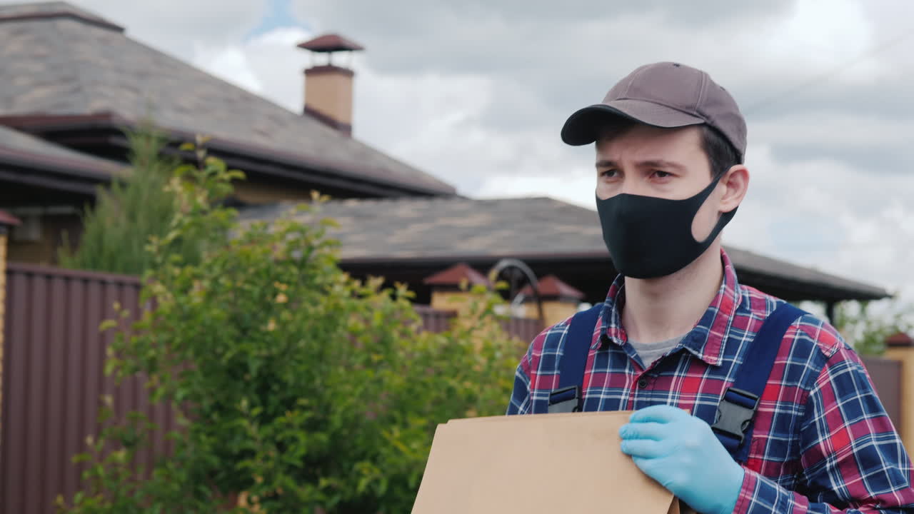 un hombre con una máscara y guantes lleva bolsas de comestibles a la casa del cliente