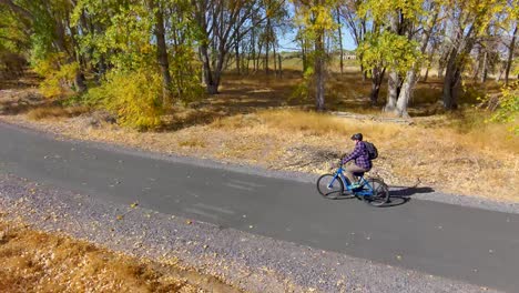 Hombre-Mayor-En-Bicicleta-A-Lo-Largo-De-Un-Sendero-Natural-En-Otoño---Vista-Aérea