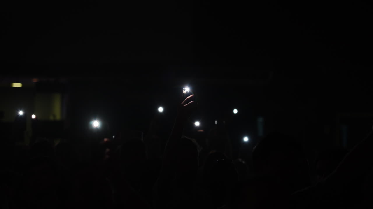 Audience holding smartphones with flashlights illuminated in a dark concert atmosphere