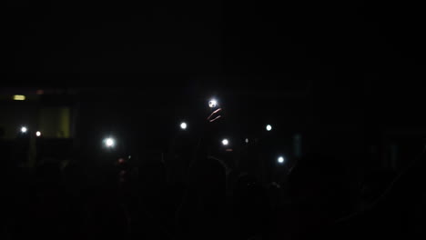 audience holding smartphones with flashlights illuminated in a dark concert atmosphere